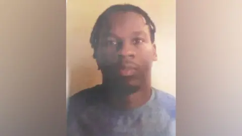 Thames Valley Police A picture of Ade Apata Omisore. He is black with short-ish hair in dreadlocks and a goatee moustache and beard. He is wearing a blue sweater and the picture is blurry.