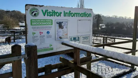 A large sign says Visitor Information, with the fencing and ground around it covered in snow