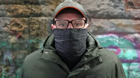 BBC man stars in camera in hat and glasses