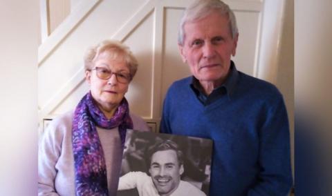 A couple hold up a photo of their dead son
