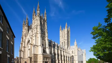 Getty Images An image of Canterbury Cathedral, a large light-stone ornate building, with a blue sky above.
