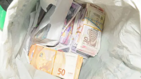 GMP Bundle of 50 and 10 euro notes as well as a roll of £20 notes police found at the cottage
