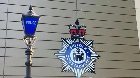 Brian Farmer/BBC It is a picture of an old police lamp post next to a Suffolk Constabulary coat of arms on a wall behind.