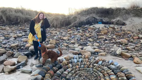 A young woman, Hannah Smith, is standing by the sculpture with her dog Cooper who is a seven month old spaniel 