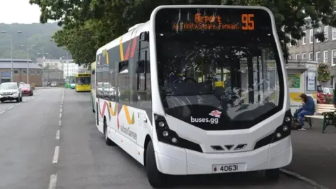 A white Guernsey bus at a leafy bus terminus. It is the 95 going to the airport.