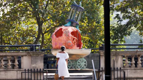theCOLAB/The Artist's Garden/Nick Turpin A woman walks up steps to the terrace. In front of her is a large sculpture.