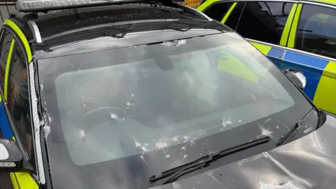 A yellow, blue and black police car with a damaged windscreen.