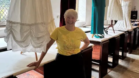St Catherine's Church A woman in a yellow T-Shirt and with short hair is standing next to a white skirt which is displayed in a church.