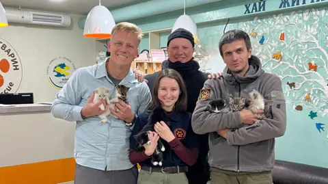 Supplied Three men and one woman standing next to each other. They are holding kittens and looking into the camera while smiling.