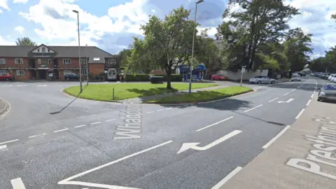 The Prestbury Road junction with Whaddon Road, in Cheltenham. It is a residential area, with red brick houses and trees. There is a dedicated lane for cars to turn right.
