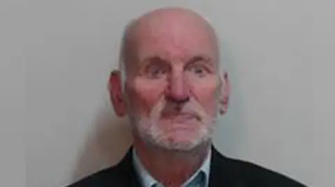 Police Scotland Brian Stobie has a bald head and a white beard. He is wearing a pale blue shirt and a dark suit jacket