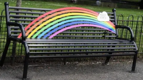 Heanor and Loscoe Town Council A metal bench with a bright rainbow and a plaque across its back rest
