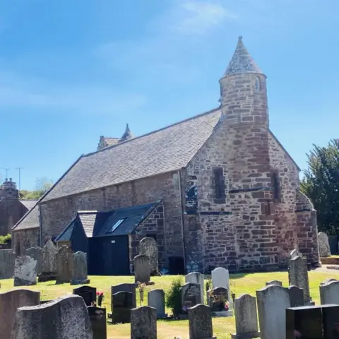 Church building - Arbuthnott Church - with graves in the foreground, under a blue sky.