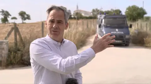 The BBC's Daniel Sandford stands in front of a road blocked by a police vehicle