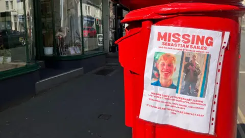 A red postbox with a missing poster for Sebastian Sailes.