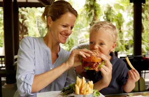 Woman feeding burger to her young son in a restaurant