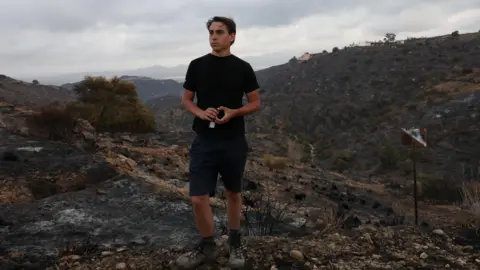 Reuters Dressed in a black t-shirt and back shorts, Thomas-Wolf Verdonckt stands on the charred landscape in Bedar, Spain, where his father was killed during the deadly wildfires. 