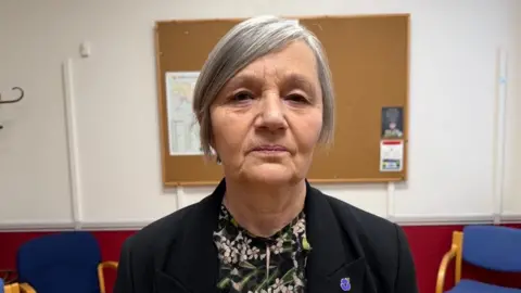 Deputy Mary Le Hegarat is wearing a black blazer and a floral top. She is pictured in a room in St Martin's parish hall.
