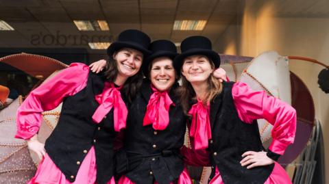 Three women dressed in top hats and waistcoats
