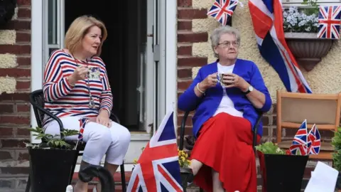 PA Two women sit outside a decorated house near Runcorn Station