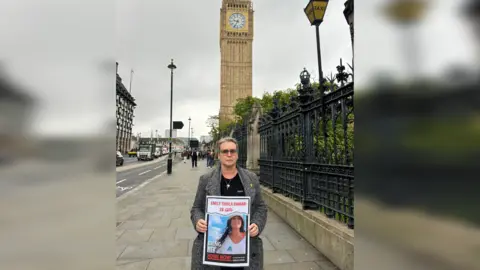 Mandy Damari A picture of Mandy Damari holding a poster calling for her daughter to be brought home