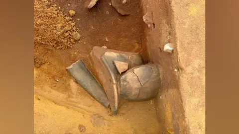 Oxford Cotswold Archaeology Bits of broken Neolithic pottery resting at the bottom of a pit excavated out of sandy soil. 
