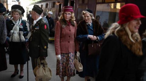 People on a heritage railway platform dressed in clothing from the 1940s and 50s