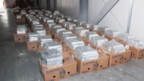 COPFS Cardboard banana boxes with silver packages on top lined up in a warehouse