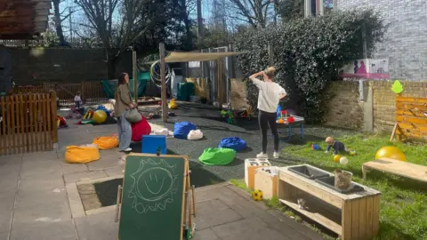 An outdoor children's playground with two mums talking and two toddlers playing 