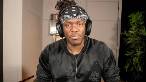 KSI wearing a black jumper and bandana with headphones.