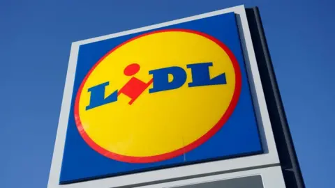 A large Lidl supermarket sign stands under a clear blue sky.