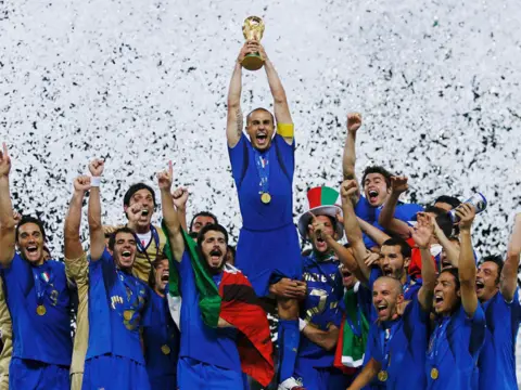 Getty Images The Italy team rejoice as a player lifts the trophy as confetti and streamers are let off behind them. Most of the team have their hands in the air as they celebrate.