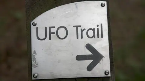 Getty Images A silver metal sign screwed to a wooden post reads "UFO Trail".