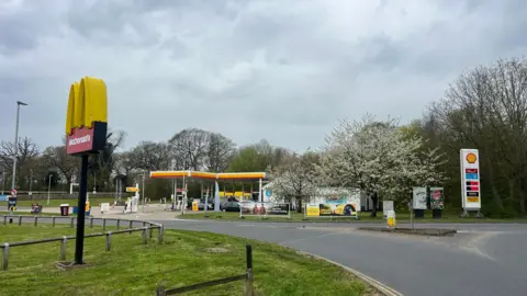 BBC/Owen Sennitt A McDonald's 'golden arches' restaurant sign can be seen in the foreground at the entrance to a service station, with a Shell petrol station in the background.