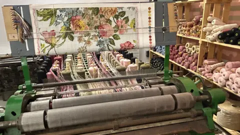 A machine is used to create fabric with a floral design in pinks and greens.