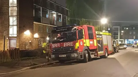 A fire engine parks next to a maisonette in the dark