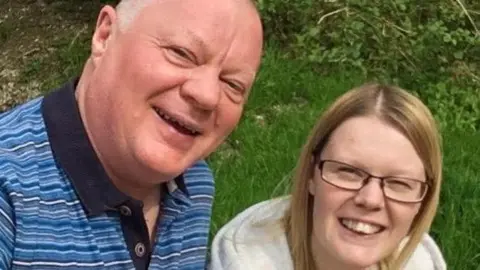 A man in a striped shirt smiles next to his daughter, who wears a grey hoodie.