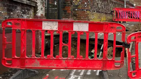 A sinkhole which has been cordoned off on Carrow Hill in Norwich. There are red plastic fence panels around the sinkhole.