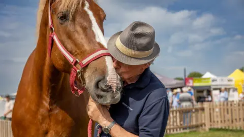 Bath and West Martin Clunes is kissing a brown horse.