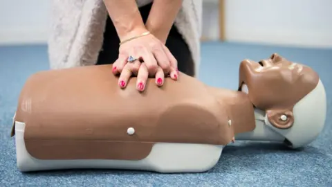 Getty Images A resuscitation dummy with a woman practicing CPR on it.