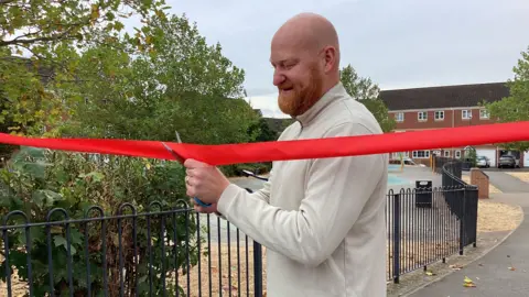 Andy Whing wearing a cream jumper smiling as he cuts a red ribbon.