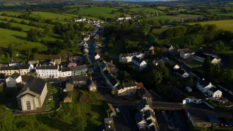 Dan Kitwood/Getty Images An aerial view of the village of Pettigo, surrounded by green fields. There is a large church in the right side of the photo which is in County Donegal. An arched stone bridge in the left of the photo marks the gateway into County Fermanagh. 