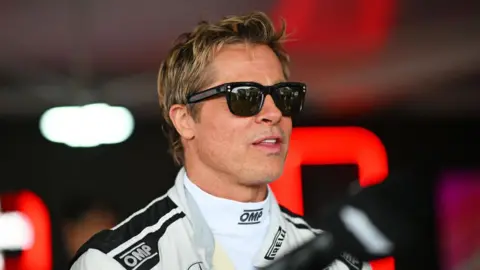 Getty Images Brad Pitt at a Grand Prix wearing dark glasses and a racing suit