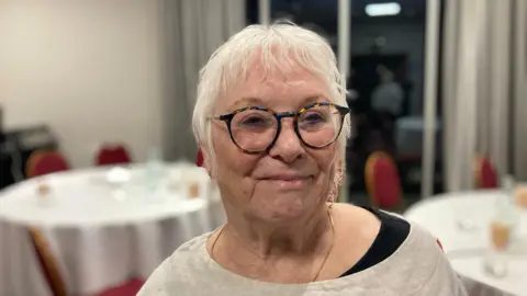 Woman wearing glasses looking at camera and smiling. Round tables in the background