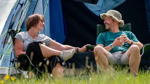 Dylan Roberts A man and a woman sit in camping chairs and smile at each other outside a large tent.