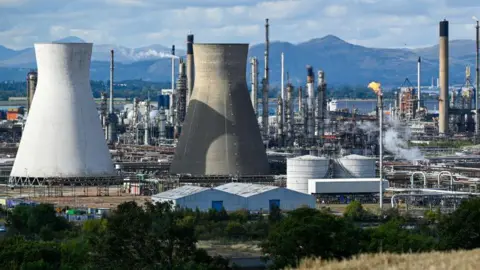 A general view of Grange mouth refinery with industrial towers, chimneys with trees mountains and water in the background.