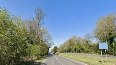 A dual carriageway runs in both directions, with grass verges in the middle and either side.