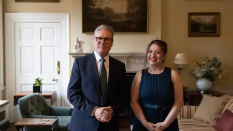 Keir Starmer, wearing a dark suit and grey tie, stood next to Silvia Marko. She is wearing a navy blue dress. The pair are in a room at Downing Street.