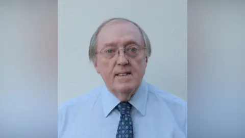 John Sweeney Prof John Sweeney has thinning grey hair and wire framed glasses. He is wearing a light coloured shirt and a spotted tie