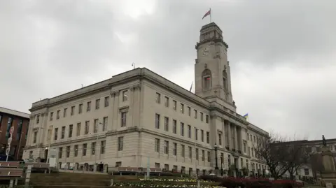 Barnsley Town Hall, a large rectangular stone building in Barnsley. It has a large clock tower with a union flag flying at it's top.